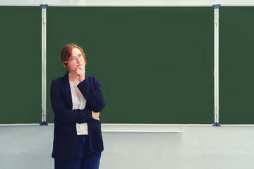 A school teacher stands doubtfully in front of an empty blackboard, copy space for the inscription....