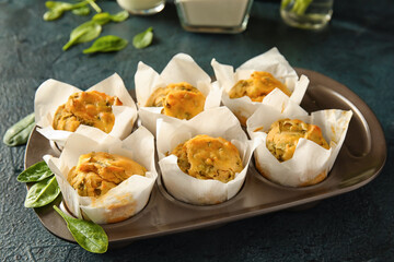 Baking tin with tasty spinach muffins on dark background