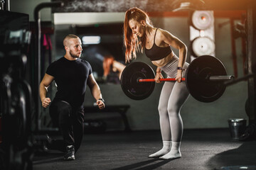 Fototapeta na wymiar Muscular Woman Doing Hard Training With Personal Trainer At The Gym