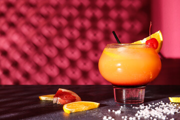 Glass of tasty Tequila Sunrise cocktail on table against color background