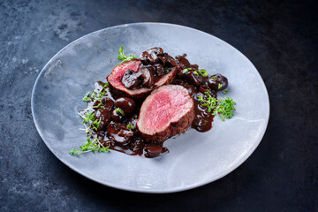 Modern style traditional fried dry aged angus beef filet medaillons natural with mushrooms in red wine sauce served as close-up on a design plate with copy space