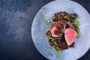 Modern style traditional fried dry aged angus beef filet medaillons natural with mushrooms in red wine sauce served as top view on a design plate with copy space left - obrazy, fototapety, plakaty