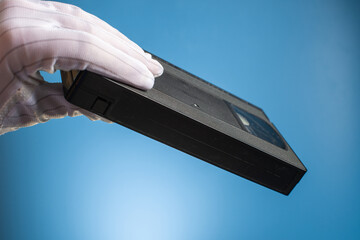 Hand holds retro HVS video cassette on a blue background. Retro wave. 80s 90s. Open film.