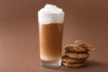 Glass of tasty latte with nuts and cookies on brown background