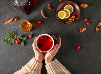 Woman holding cup of tasty rose hip tea on black background