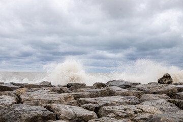 Fototapeta na wymiar Waves crashing over rock wall on lake Michigan in Kenosha, stone wall with clouds during a gale-force storm along the Wisconsin coastline causing flooding and damage to harbors and Marinas