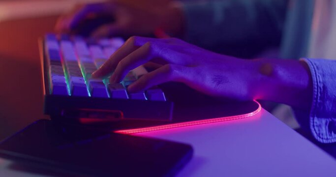 Close-up hands shot asia guy gamer use keyboard and mouse controller play video game with neon light computer in desk at home. Online esport streaming game online, Home quarantine activity concept.