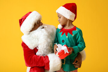 Cute little elf with gift and Santa Claus on yellow background