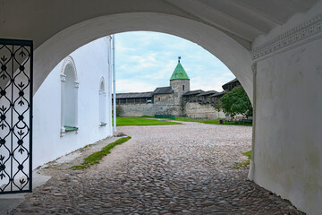 a look through a wide arch at the fortress wall and watchtower of the Pskov Kremlin. Russia