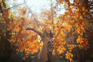 smiling modern female in beige coat and orange hat rejoicing