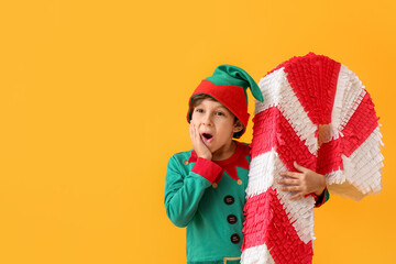 Cute little boy dressed as elf with candy cane pinata on color background