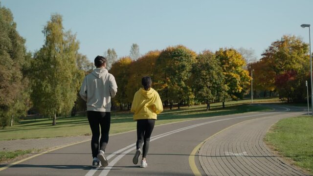 Man and woman start running on a track at the city park in sunny autumn morning. Couple of young people starting a morning run. Running with a partner talking. High quality 4k footage