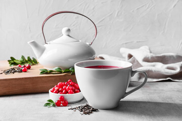 Cup of tasty lingonberry tea, berries and teapot on table