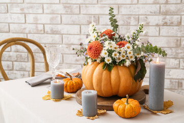 Beautiful bouquet of autumn flowers in pumpkin on served table near brick wall