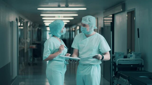 Two surgeons are discussing papers in the hallway