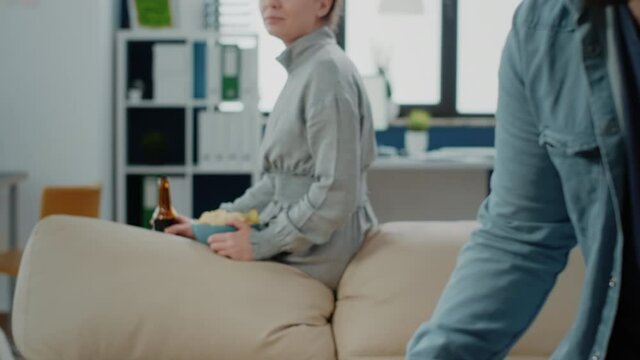 Portrait of woman with chips and bottle of beer after work, watching coworkers play game on foosball table. Person enjoying drinks and snacks to celebrate with fun activity after hours