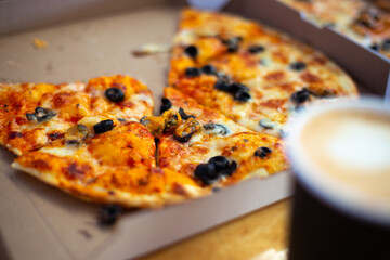 Fresh pizza cut into pieces in a box on the table, blurred focus