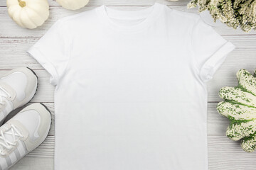 White womens cotton t-shirt mockup with pumpkins and sneaker on white wooden background. Design t...