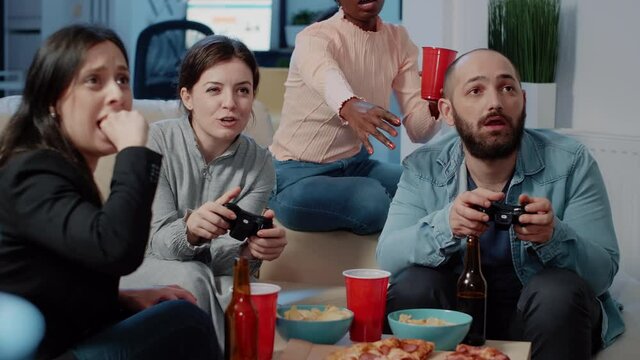 Close Up Of Colleagues Playing Video Games On Console, Enjoying Drinks And Snacks After Work. Coworkers Having Fun With Game And Controllers While Using Television After Hours.