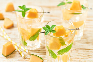 Melon lemonade with ice and mint in a glass on a wooden table. Melon drink in glasses with melon slices. melon water in glass jars.