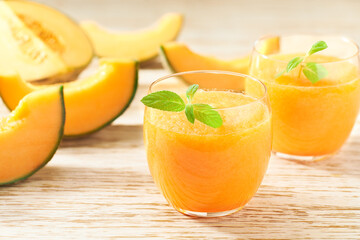 two glasses of melon smoothie with fresh cantaloupe melon and mint on a wooden table.