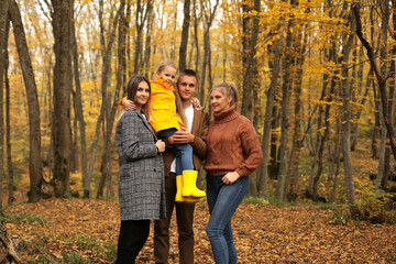 a young handsome guy in an autumn beige jacket is holding a little girl in a yellow raincoat next to young beautiful girls are standing autumn city forest park