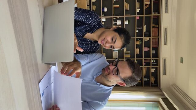 Friendly colleagues business partners of diverse gender race sit by laptop at office workplace discuss work prepare report. Young indian woman expert consult man apprentice help in job. Vertical video