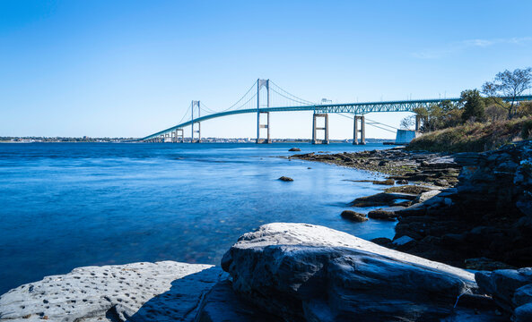 Tranquil wintry seascape with the view of Claiborne Pell Newport Bridge and rocky beach on Route 138 in Rhode Island. Smooth water flows under the bridge, long exposure photography.