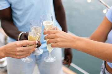 Group of multiracial friends clinking and toasting with glasses of champagne on party boat - Mixed race people celebrating together having drinks at party outdoors - Focus on champagne glasses hands