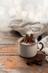 Obraz na płótnie Canvas A mug of hot chocolate or cocoa with cinnamon sticks on a wooden table. Warm scarf and cozy autumn winter concept. Blurred bokeh in the background.