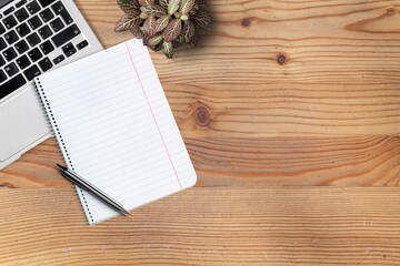 Blank notebook with pen on an office desk table with laptop computer, and supplies.