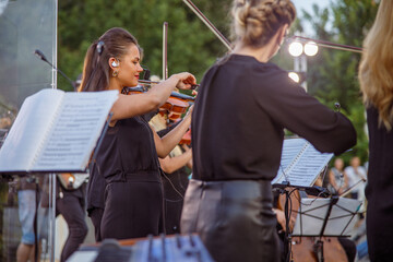 Beautiful woman violinist playing in orchestra on the street