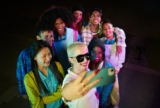 Group Of Friends Taking Selfie With Mobile Phone Having Fun At The Party At Night. Crowd Of Happy Multiethnic People