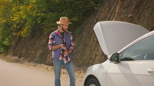 Sad hipster young bearded caucasian frustrated man opening car hood, standing on empty rural road and waiting for help. Emergency situation. Stress. Car troble. Car breakdown.