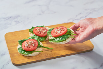 Hand holding Healthy snack of rice cakes with spinach and tomato on top.