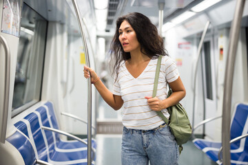 Asian woman with shoulder bag standing in subway train and holding handrail.