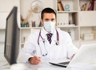 Experienced male therapist wearing surgical mask holding consultation in clinic office