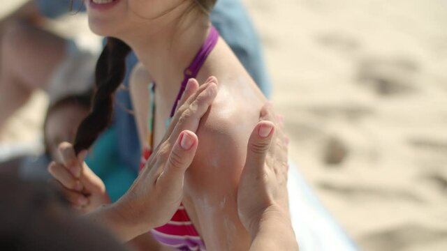 Close-up shot of moms hands applying sunblock on kids shoulder. Caucasian mother putting sunscreen on daughters skin during summer vacation at sea, taking care of health. Skincare, family concept