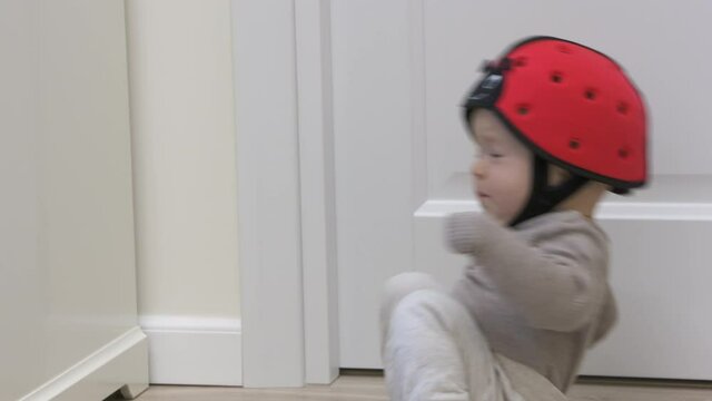 Baby boy wearing soft safety helmet falls backwards and hits his head on the floor, child crying lying on his back, head protector helps reduce impact of fall. High quality 4k footage