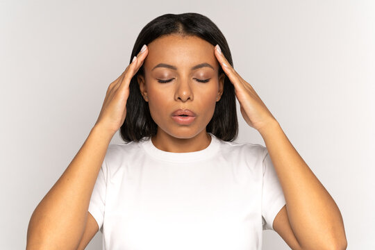 Stressed young woman massaging temples and breathing in deeply to relief from emotional stress, anxiety or disorder. Anxious female with closed eyes touching head suffer from hard headache or migraine