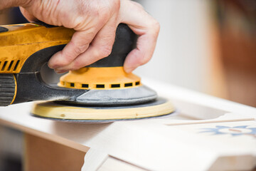A man using a power tool electric sander to craft wood in the carpentry trade