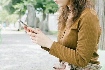 公園で携帯電話を操作する女性　
笑みを浮かべて携帯を操作する女性　