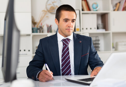 Portrait of confident focused office employee during daily work with laptop and documents