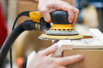 A man using a power tool electric sander to craft wood in the carpentry trade