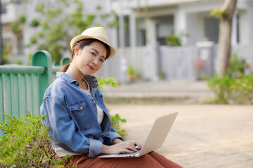 Young woman with laptop sits on couch in the park on a sunny day.