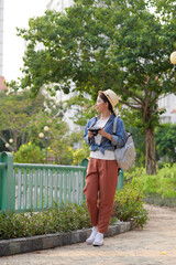 Young beautiful Asian backpack traveler woman using digital compact camera and smile, looking at copy space