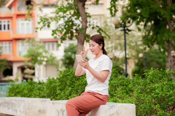 Confident young female student sitting on phone In park freely And intend ready in sun during sunset happy that day