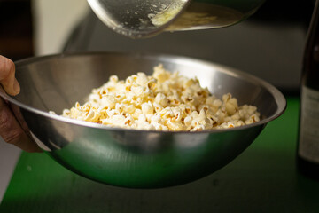 A male hand pours butter on popcorn and shakes the bowl