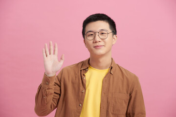 Portrait of Asian man in blue t-shirt raising hand up and welcomes with a palm and smiles