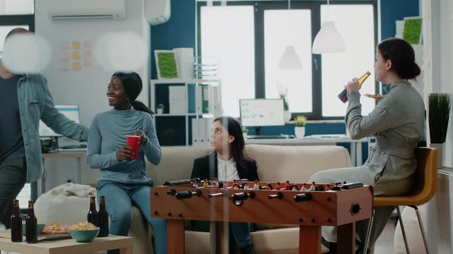African american woman playing at foosball table with man after work at office. Workmates enjoying football play while having drinks and snacks after hours to have fun and entertainment